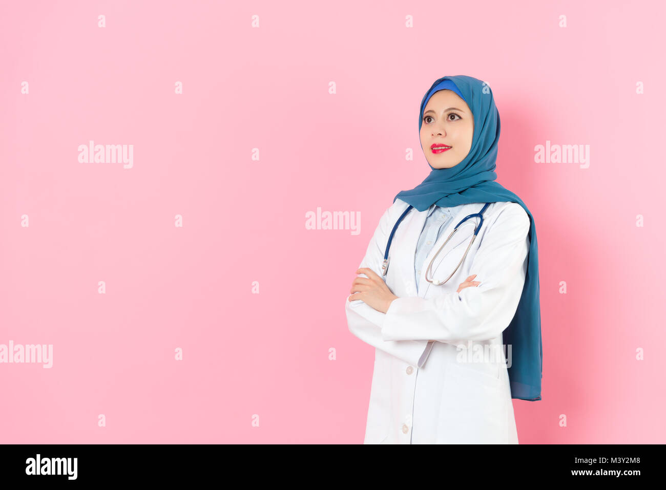 Lächelnde junge muslimische Frau Doktor die Hände auf der Brust gekreuzt entspannende und stehen in rosa Hintergrund auf der Suche nach leeren Bereich Träumen. Stockfoto