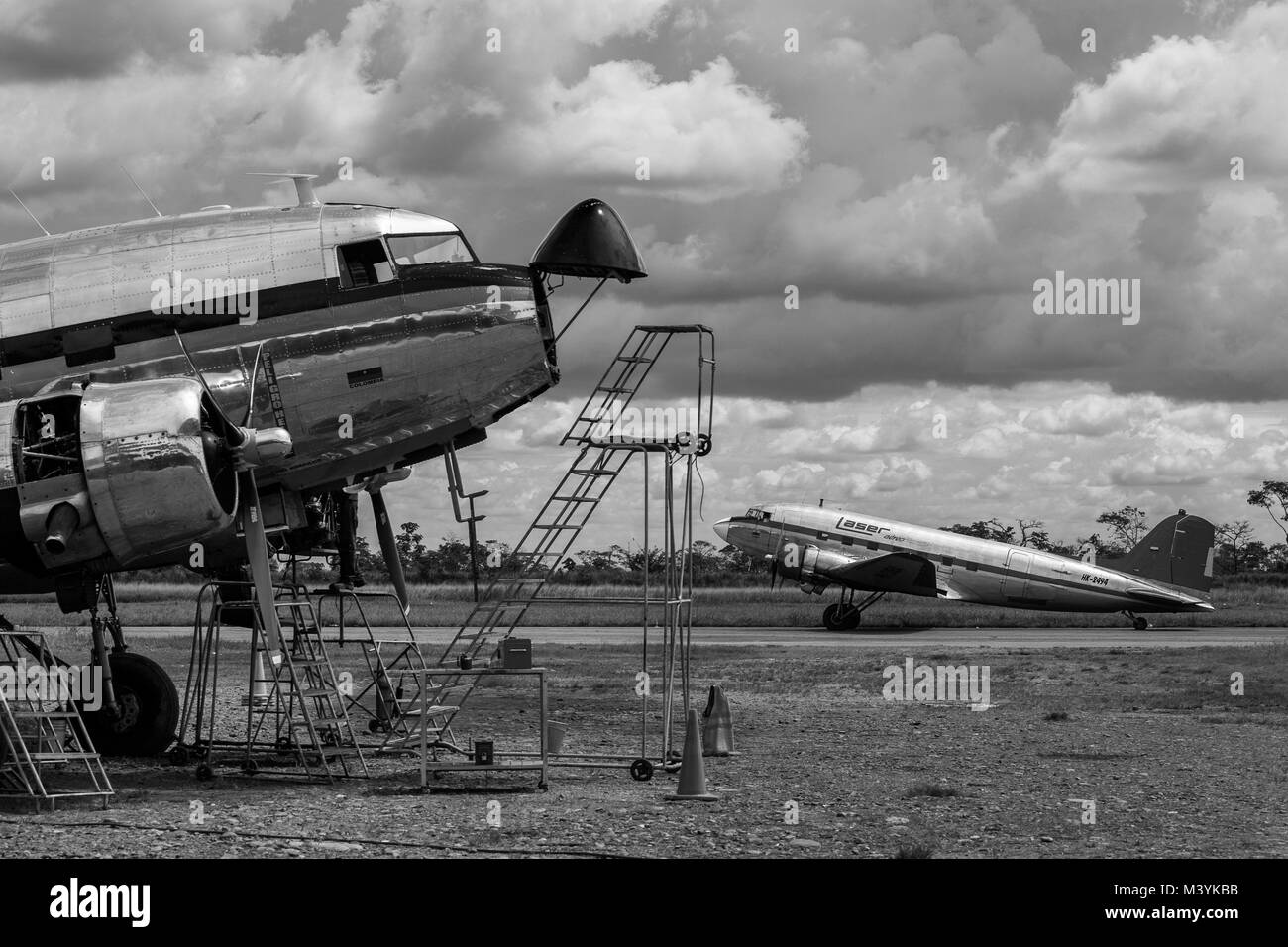 Eine Douglas DC-3-Flugzeug, Allas Airlines betrieben, geparkt bei einer routinemäßigen Wartung prüfen, während eine Douglas DC-3-Flugzeug durch Laser Airlines betrieben, am Flughafen von Villavicencio, Kolumbien, 5. Dezember 2016 stattfindet. Obwohl die meisten der Flugzeuge der DC-3 Serie wurden 1940 erbaut, heute, fast 80 Jahre nach, einige von Ihnen noch weiterhin im täglichen Dienst zu fliegen, fahren die endlosen Savannen und Dschungel im im Südosten von Kolumbien. Transport von Menschen, Lebensmittel, Tiere oder sogar kleine Fahrzeuge, ein legendäres amerikanisches Flugzeug ist manchmal die einzige Verbindung zw. Stockfoto