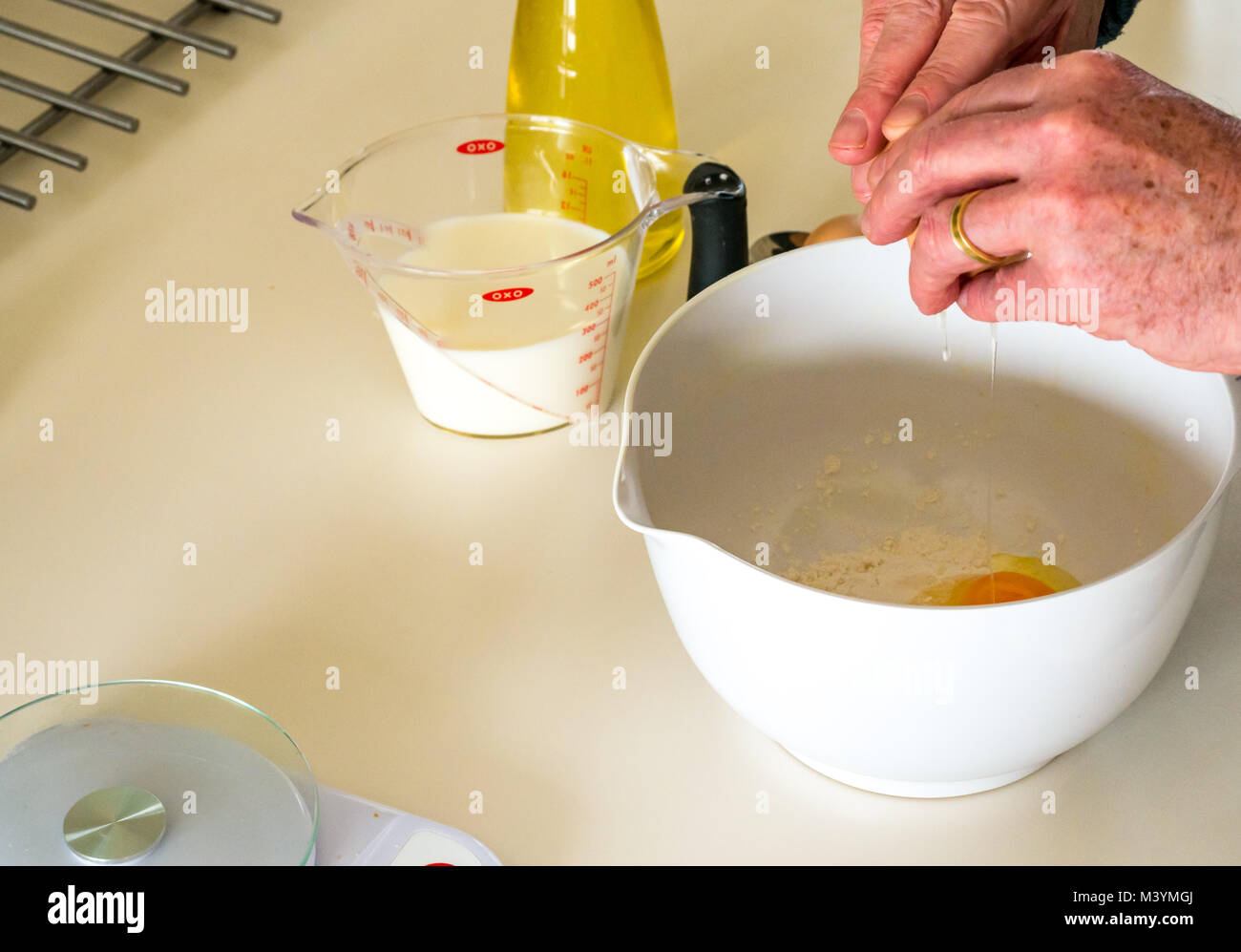 Mann schlagen Mischung mit Schneebesen Pfannkuchenteig für Faschingsdienstag mit Mehl, Milch, Eier und Öl in einer Küche zu Hause Stockfoto