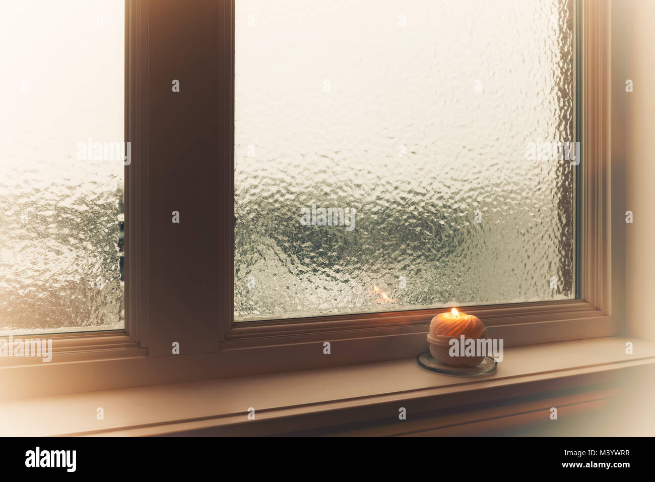 Brennende Kerze und gefrostet Fenster im dunstigen Licht. Winter Zusammensetzung. Stockfoto
