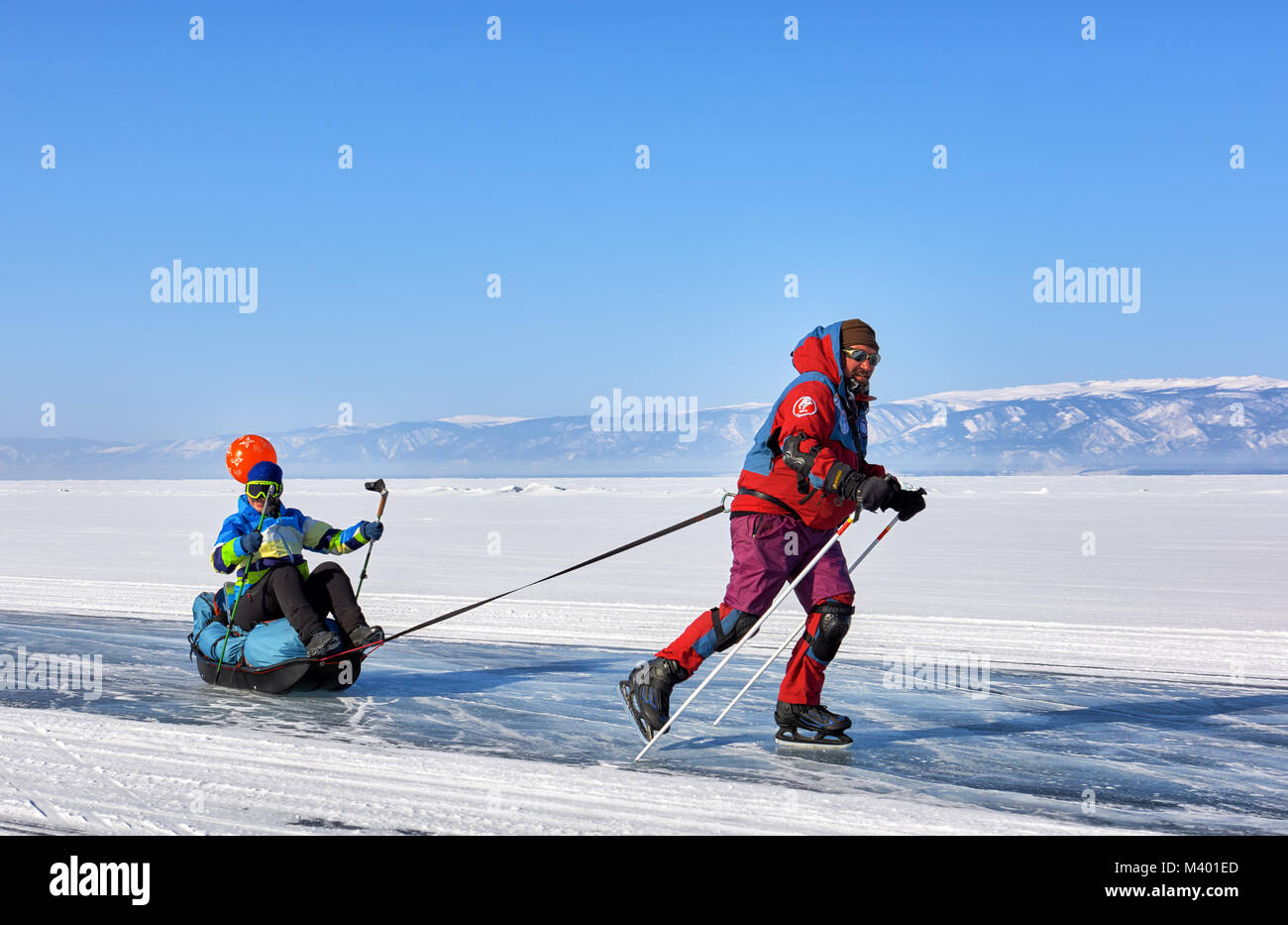 Baikalsee, Irkutsk Region, Russland - März 08, 2017: Zufriedene Mann rollt Frau sitzt im Schlitten ziehen. Fröhliche aktive Erholung im Winter in Sibirien Stockfoto