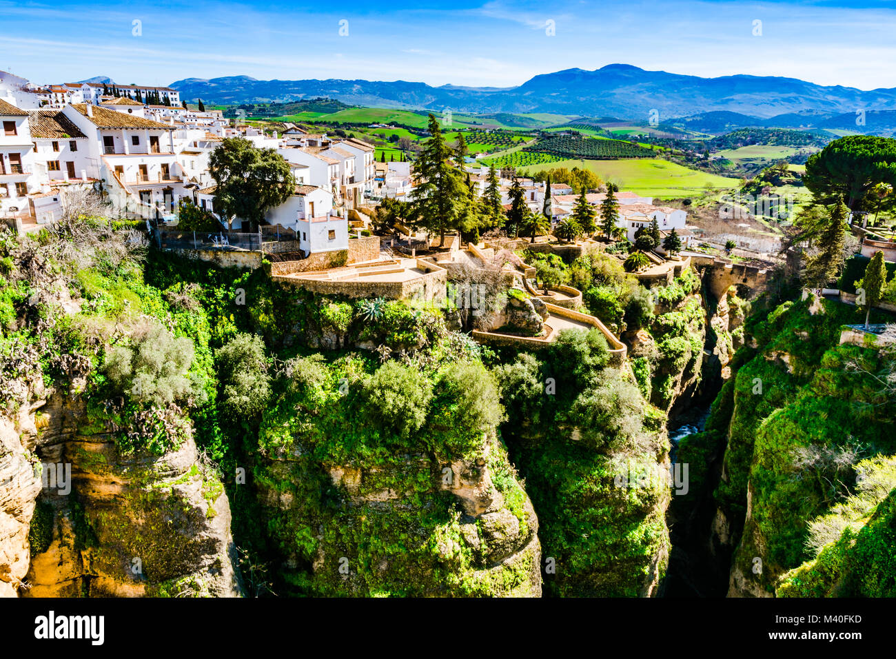 Ronda, Spanien: Landschaft der Weißen Haus Am grünen Rand der steilen Klippen mit Bergen im Hintergrund. Stockfoto