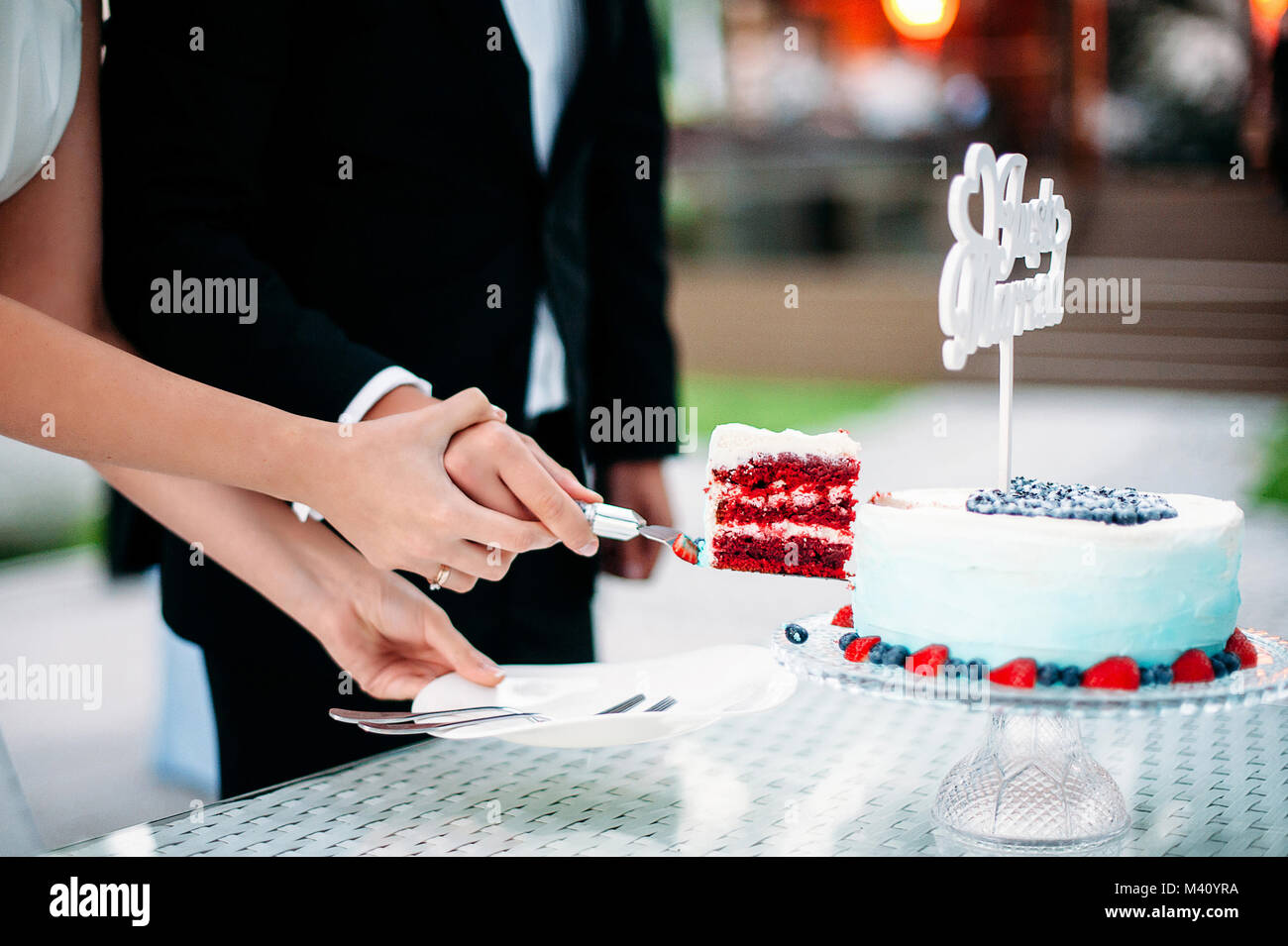 Die Jungvermählten schneiden Sie ein Stück Hochzeitstorte aus rotem Samt. Weißen und Blauen Gradienten Kuchen mit Schild Just Married, Dekoration mit Blaubeeren und Erdbeeren Stockfoto