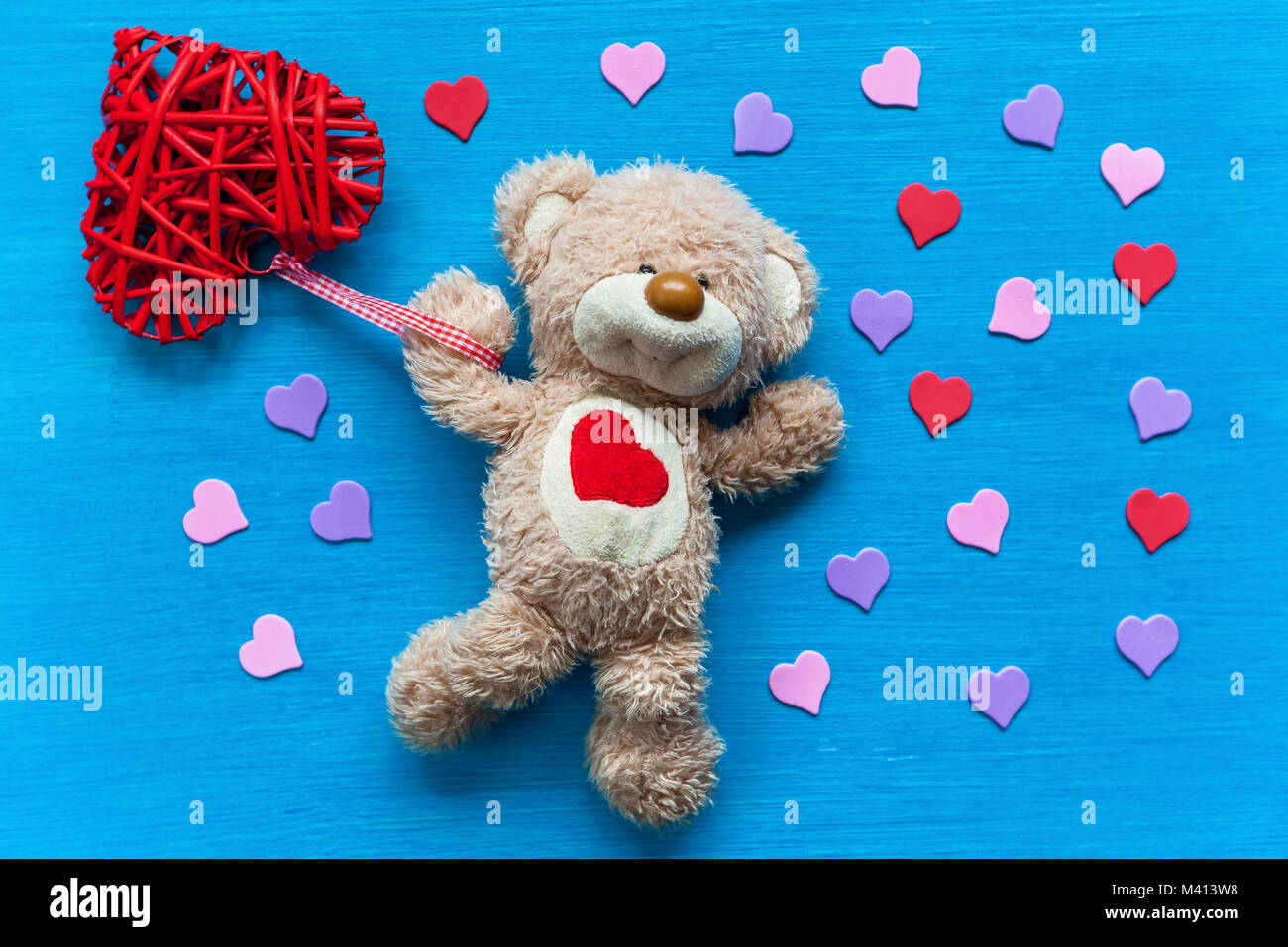 Beige, Teddybär liegt auf einem türkisfarbenen Tisch und hält ein Herz. Bär  mit Herz Stockfotografie - Alamy