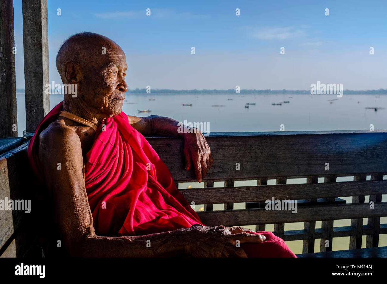 Eine alte, buddhistischer Mönch sitzt auf U-Bein Brücke aus Teakholz, eine alte Brücke, Blick über den See Taungthaman Stockfoto