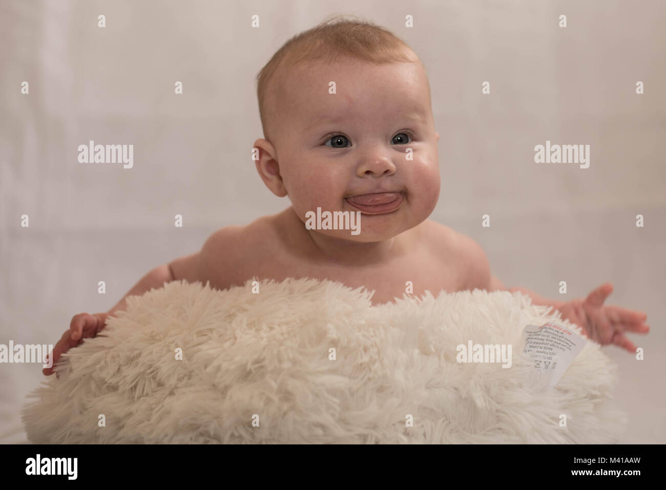 Cute Baby mit weißem pom pom Hut auf dem schaffell Teppich Stockfoto
