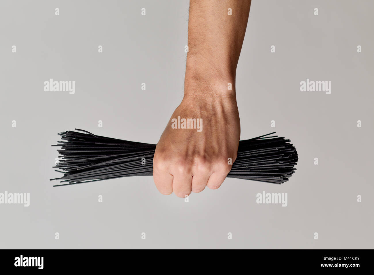 Nahaufnahme eines jungen kaukasischen Mann mit einem Bündel ungekocht schwarze Spaghetti in seine Hand gegen einen weißen Hintergrund Stockfoto