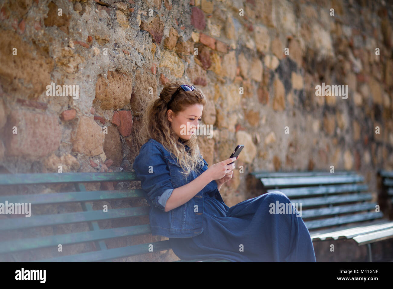 Junge erwachsene Frau mit Smartphone, auf einer Bank sitzen Stockfoto Junge erwachsene Frau mit Smartphone, auf einer Bank sitzen Stockfoto
