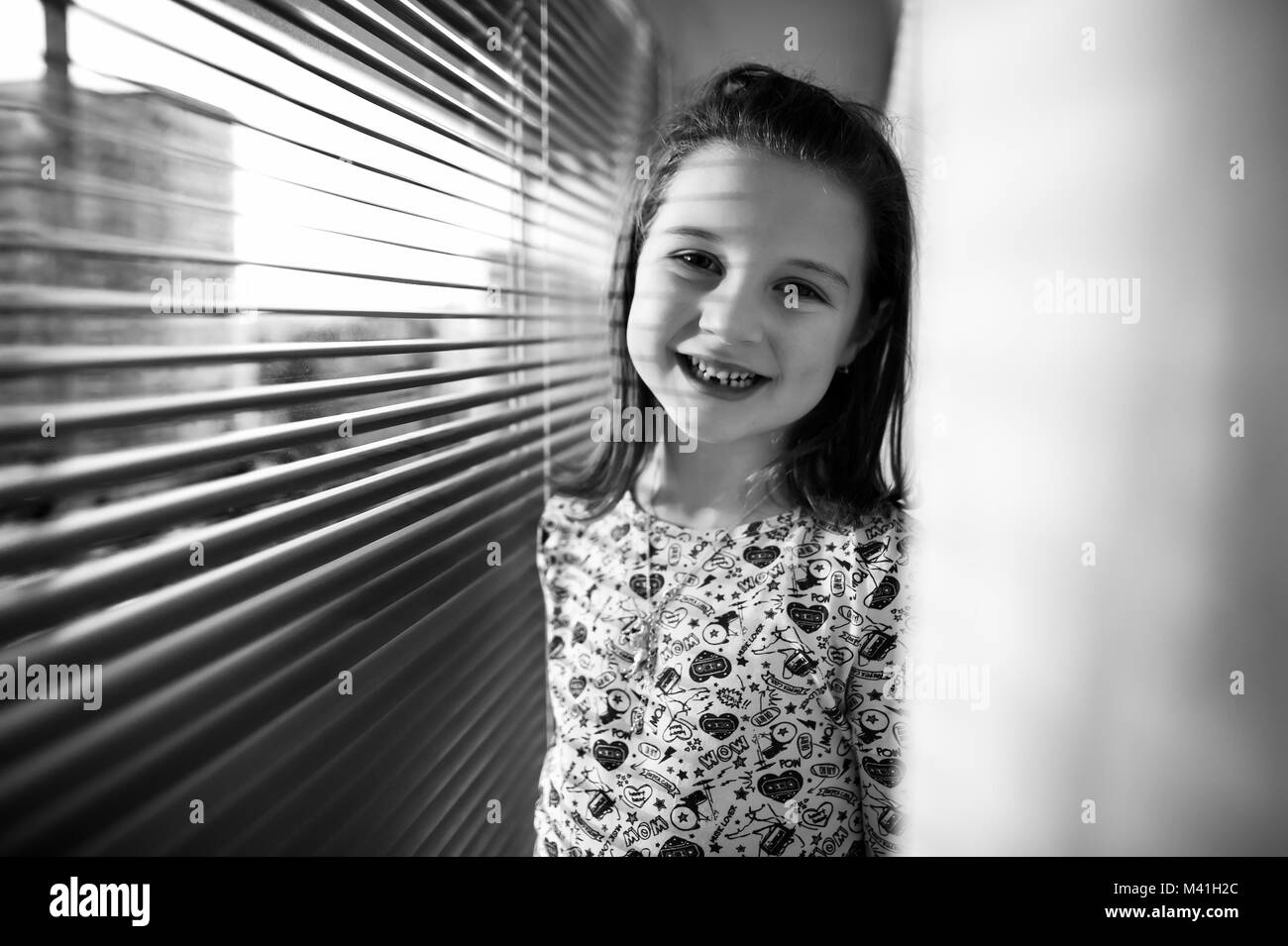 Lächelnde Mädchen neben dem Fenster mit Lamellen Stockfoto