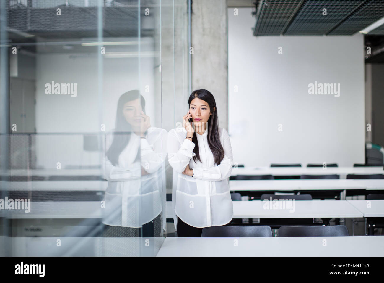 Geschäftsfrau, die an der Reflexion und Smartphone in einem Büro Stockfoto