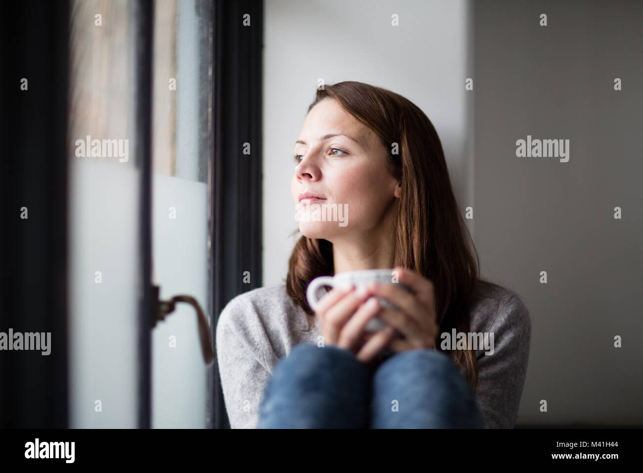 Junge erwachsene Frau in Kaffee am Morgen und Suchen aus dem Fenster Stockfoto