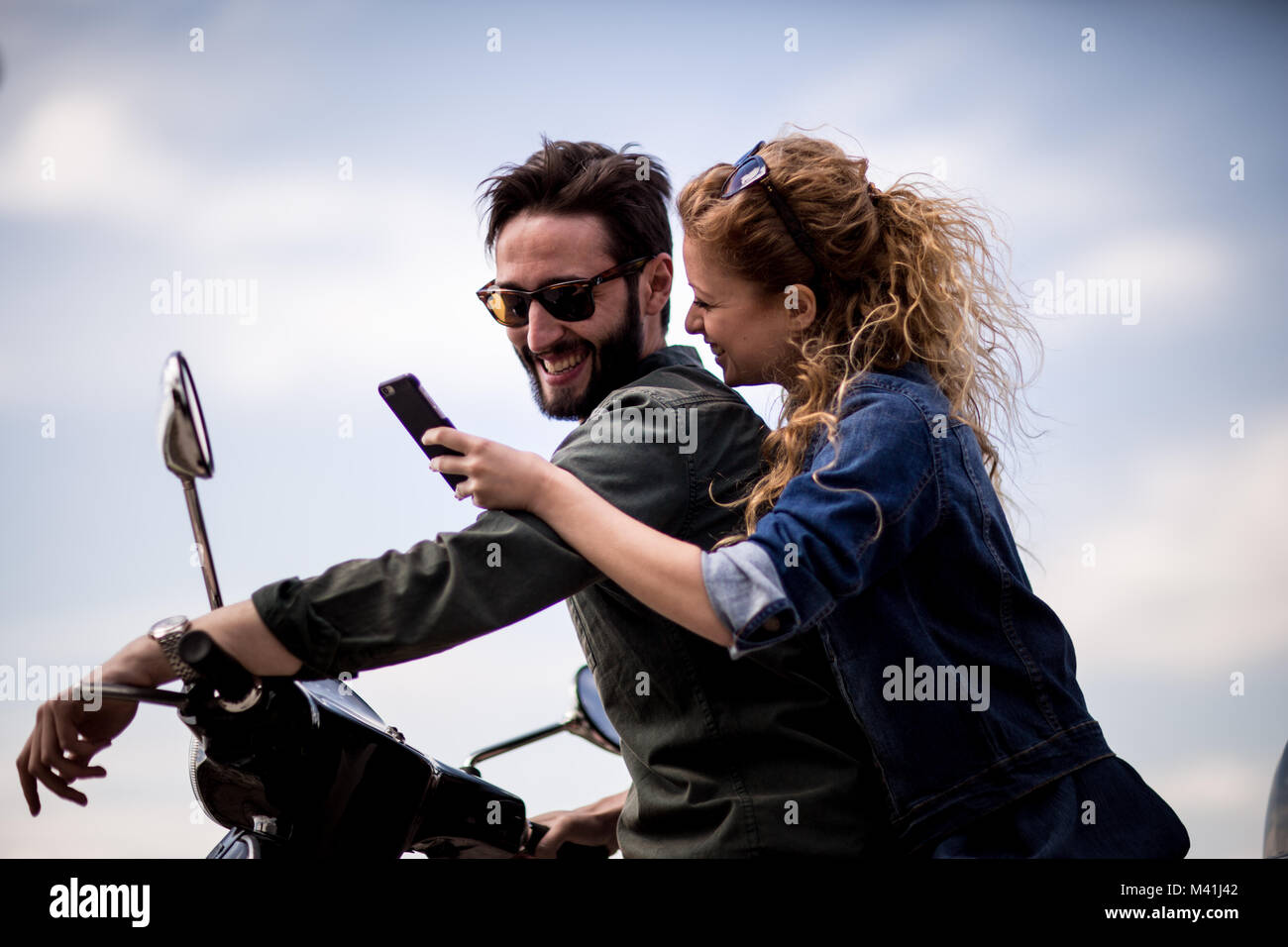 Junges Paar auf dem Motorrad zusammen mit Blick auf Smartphone Stockfoto