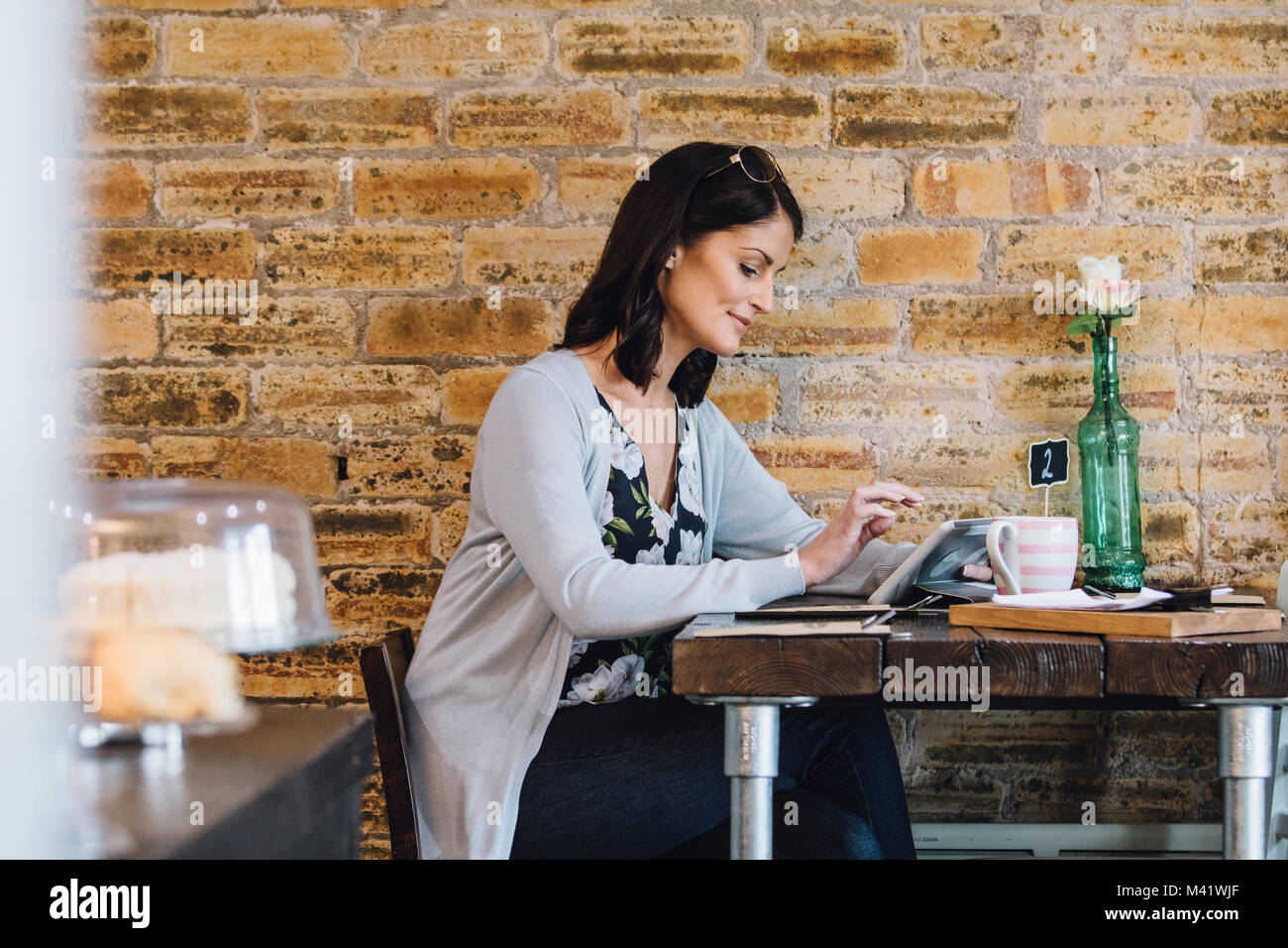 Frau ist allein sitzen an einem Tisch in einem Cafe, mit einem digitalen Tabet und genießen Sie eine Tasse Tee. Stockfoto