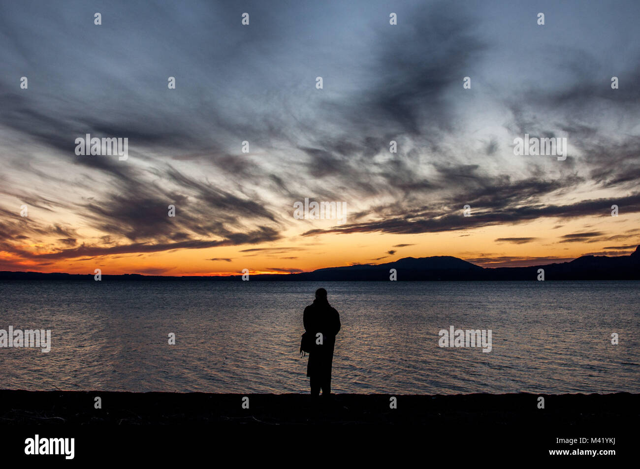 Die Silhouette einer Person alleine steht vor einem See bei Sonnenuntergang Stockfoto