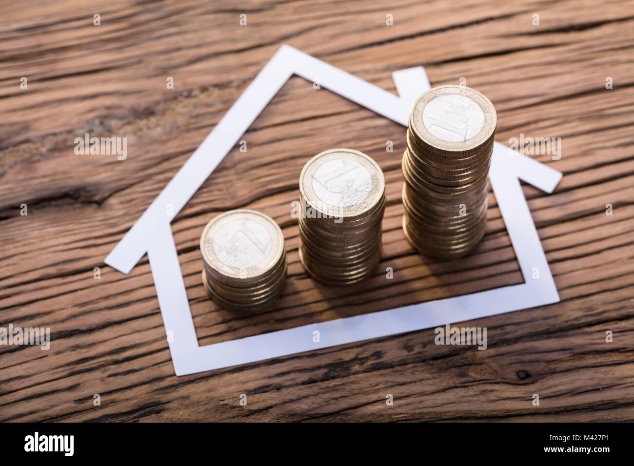 Hohe Betrachtungswinkel von Gestapelte Münzen in Papier schneiden Haus auf hölzernen Schreibtisch Stockfoto