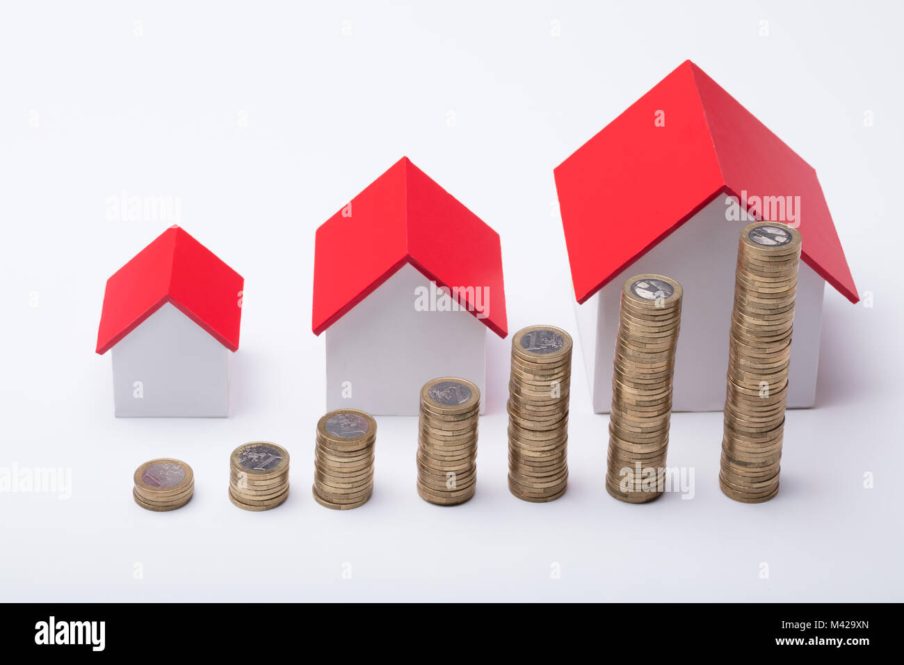 Hohe Betrachtungswinkel unterschiedlicher Größe Häuser mit Stapel von Münzen auf weißem Hintergrund Stockfoto