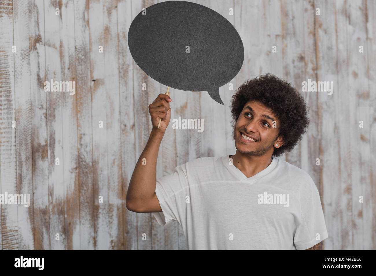 Positive Gedanken. Attraktiver mann Mulatte mit lockigem Haar mit leeren Sprechblasen und es beim Stehen gegen alte Holzwand Stockfoto