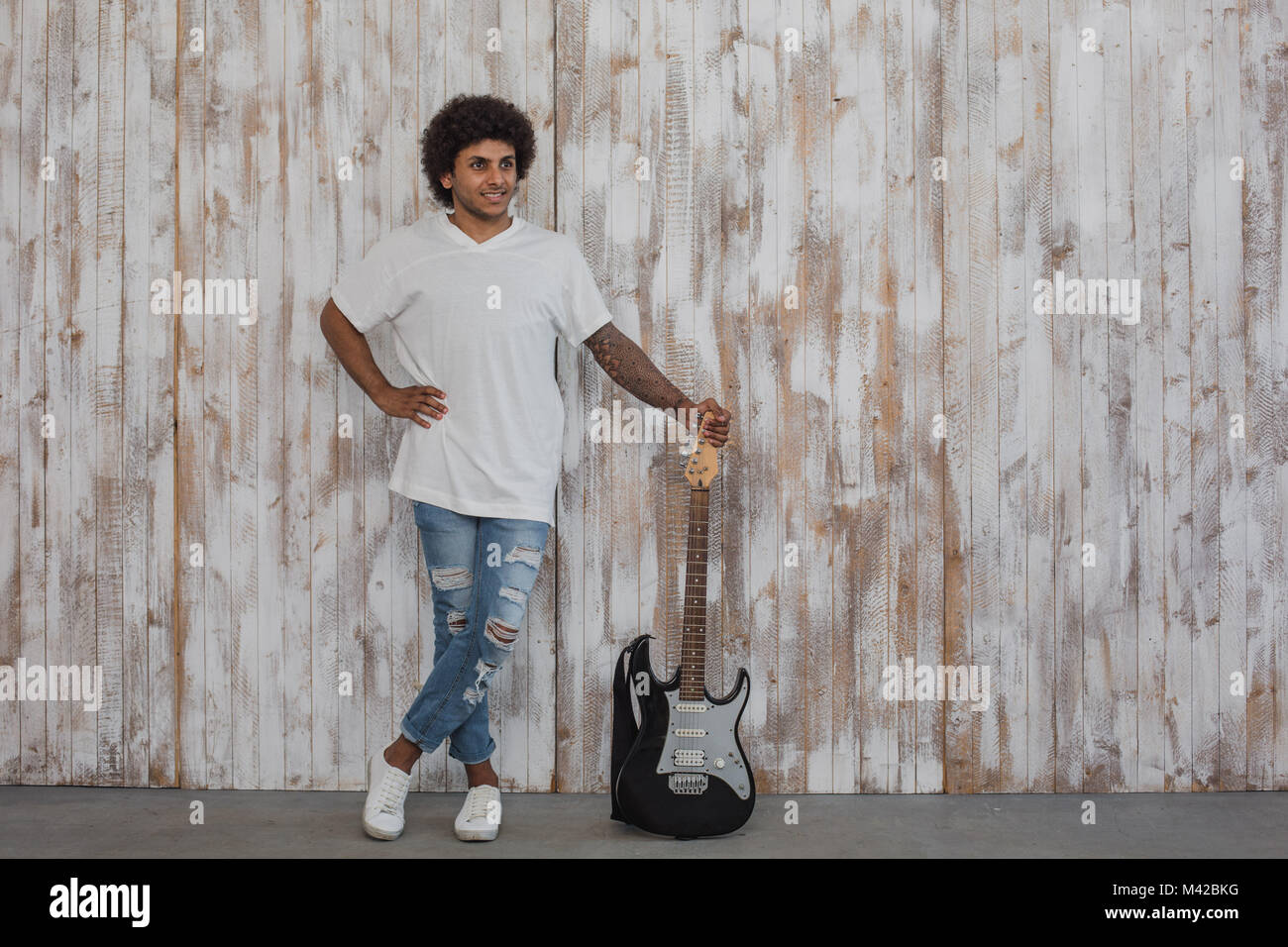 Kreative Person. Mulatte mann Musiker, mit lockigem Haar steht in der Nähe der Bass Gitarre, gegen retro Holzwand Stockfoto