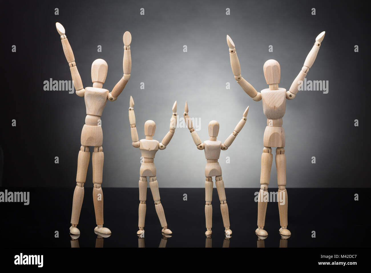 Holzfigur Eltern und Dummy Kinder heben Ihre Arme auf grauem Hintergrund Stockfoto