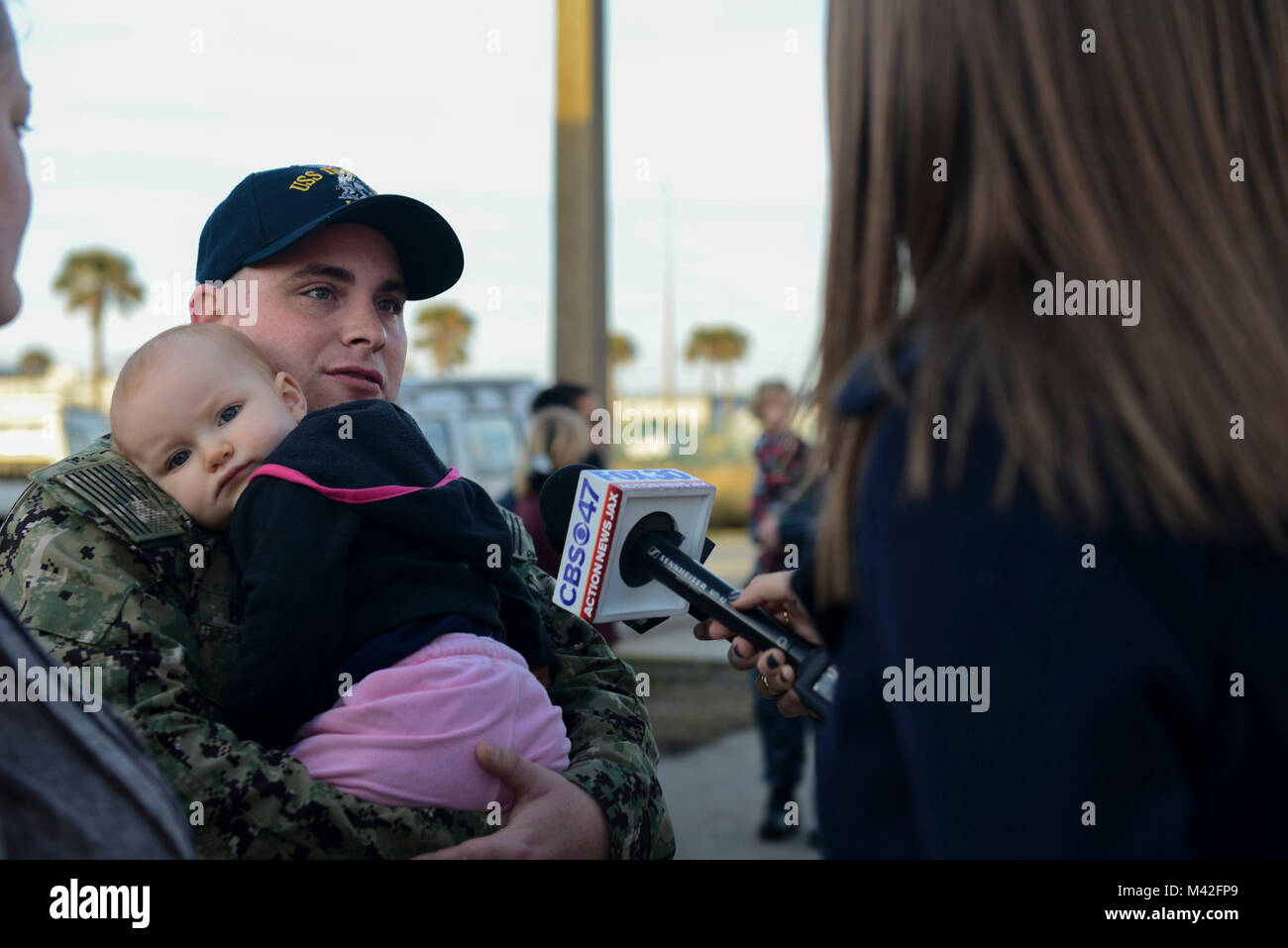 MAYPORT, Fla (Feb. 7, 2018) der Luftfahrt Bootsmann Mate (Kraftstoff) 3. Klasse Zachary Bollinger gibt ein Interview, während seine Tochter Holding vor dem Amphibisches Schiff USS Iwo Jima (LHD7) fährt Naval Station Mayport für eine Bereitstellung zur Unterstützung der Maritime Security Operations und Theater Sicherheit Zusammenarbeit in Europa und im Nahen Osten. Die Iwo Jima Amphibious Ready Gruppe begibt sich die 26 Marine Expeditionary Unit und umfasst die Iwo Jima, die amphibious Transport dock Schiff USS New York (LPD-21), das Dock Landung Schiff USS Oak Hill (LSD 51), Flotte Op-Team 8, Hubschrauber Sea Co Stockfoto