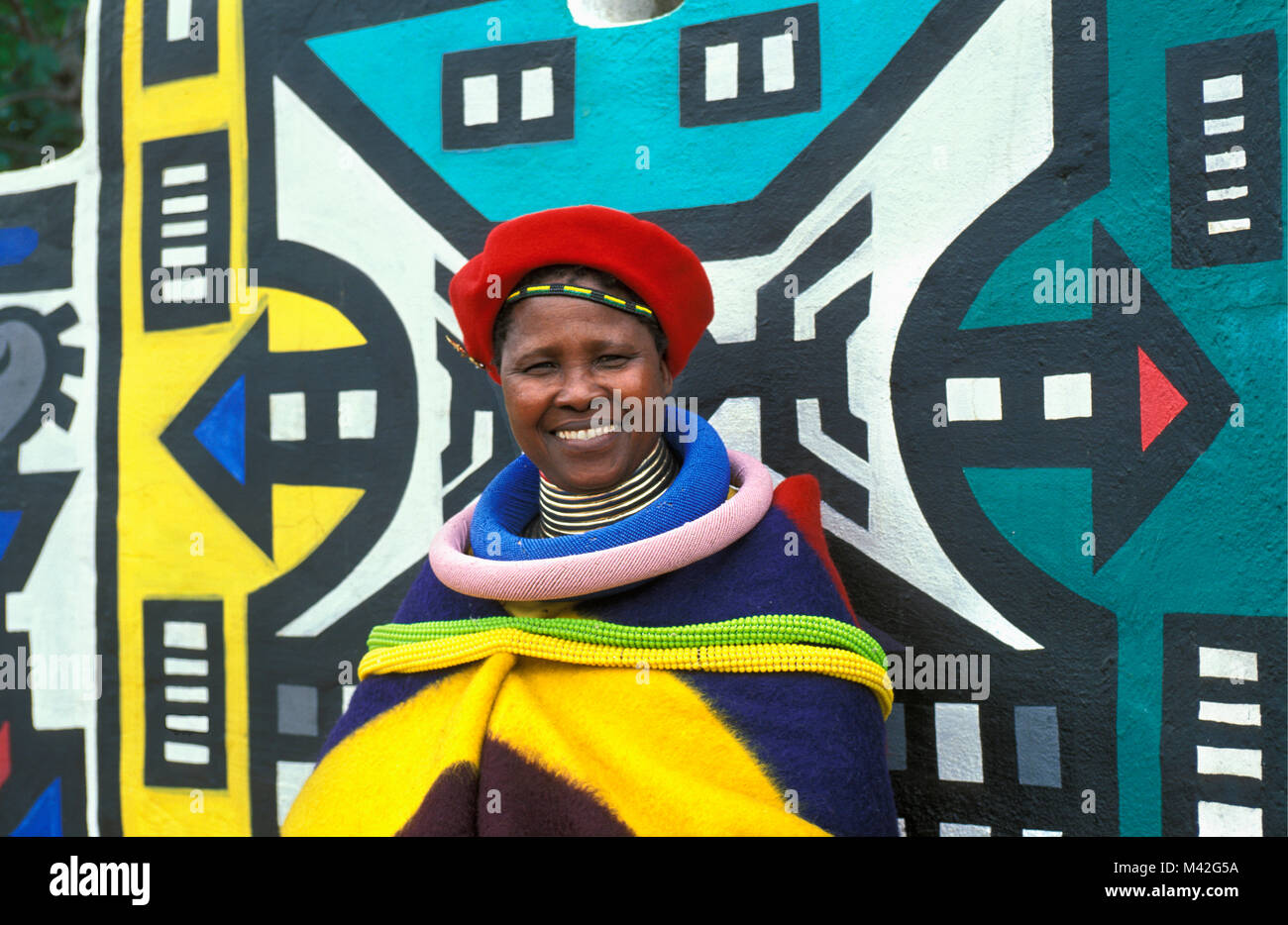 Südafrika. Mapoch Ndebele Dorf, in der Nähe von Pretoria. traditionelle Wandmalereien der Ndebele Stamm. Frau mit traditionellen Kleidung. Stockfoto