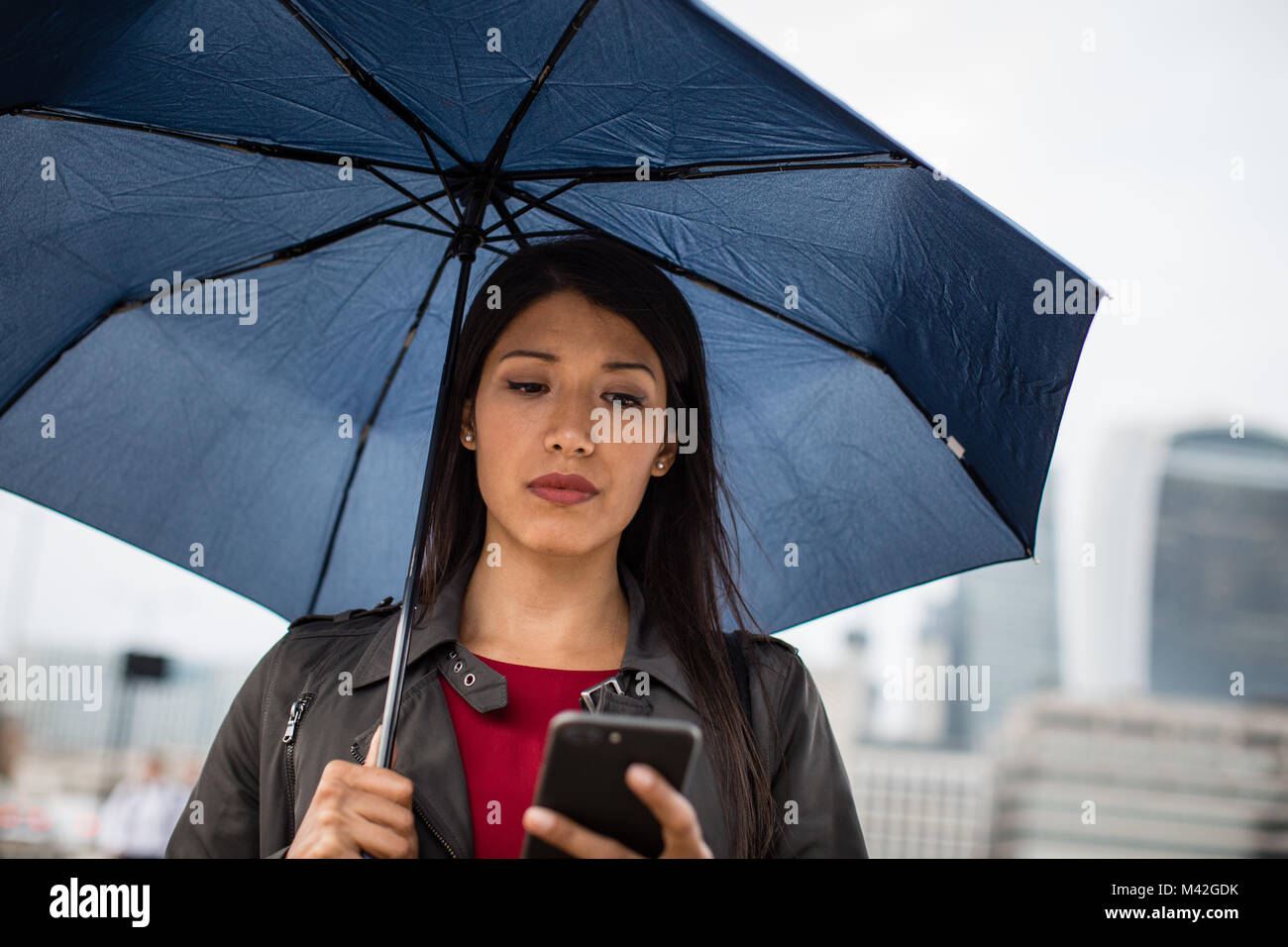 In der Stadt Holding umbrella Geschäftsfrau am Smartphone suchen Stockfoto