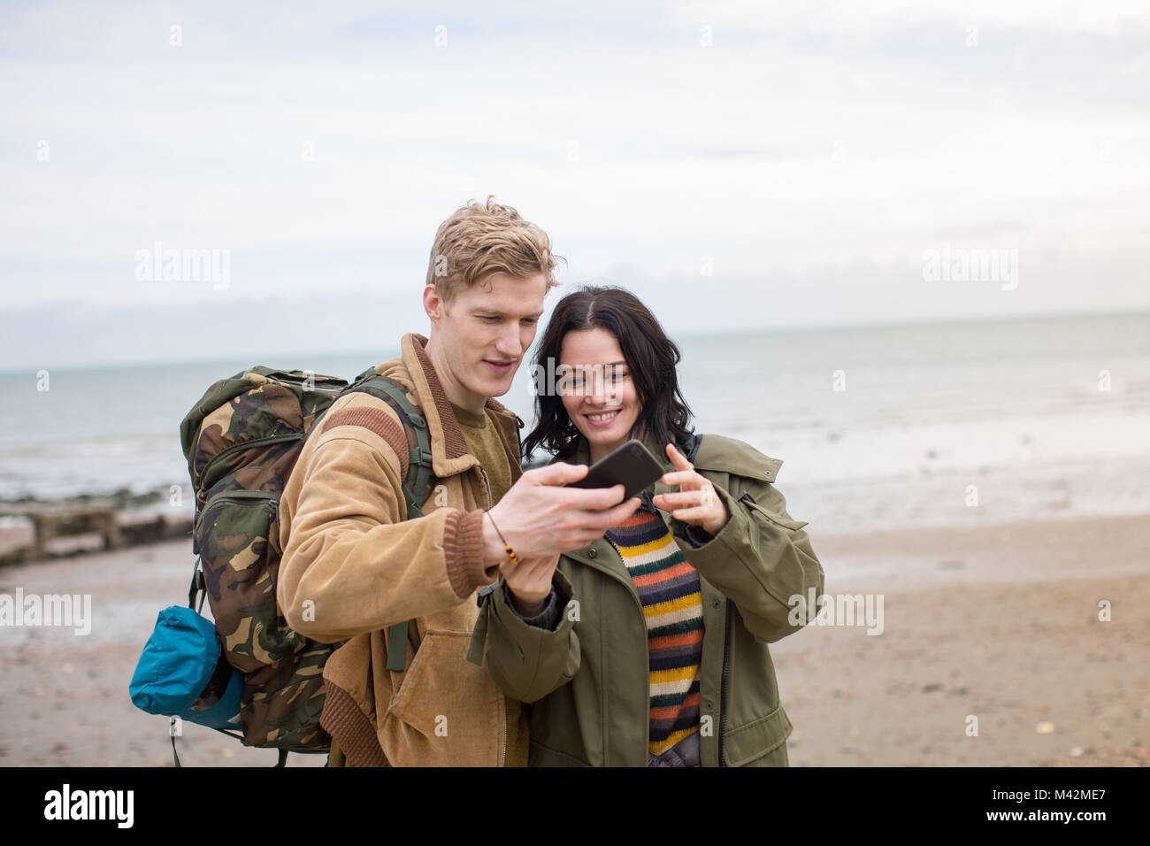 Junges Paar mit Smartphone auf einen Winterurlaub am Strand Stockfoto Junges Paar mit Smartphone auf einen Winterurlaub am Strand Stockfoto
