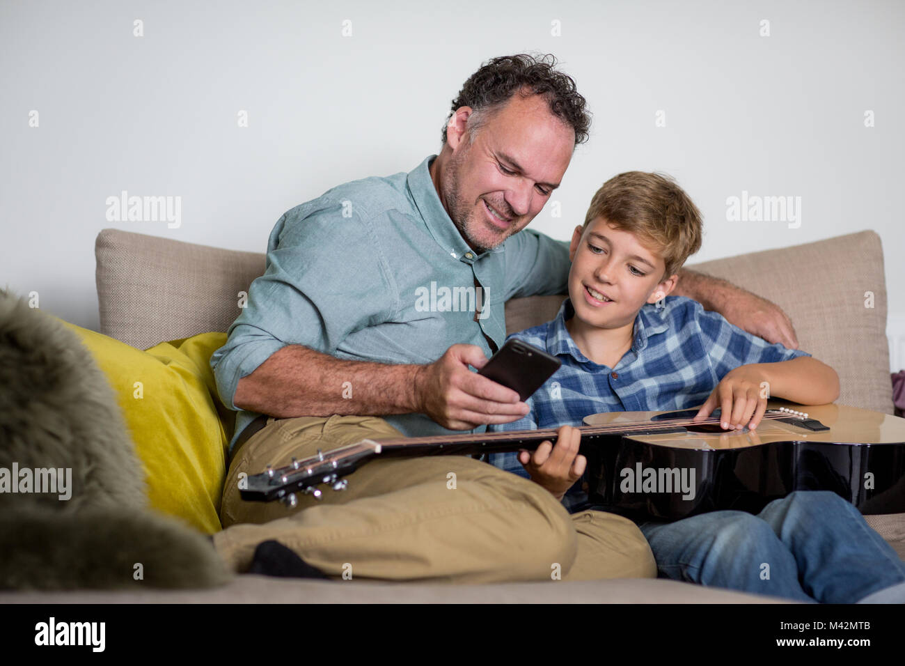 Vater lehre Sohn wie mit einem Smartphone Gitarre zu spielen. Stockfoto