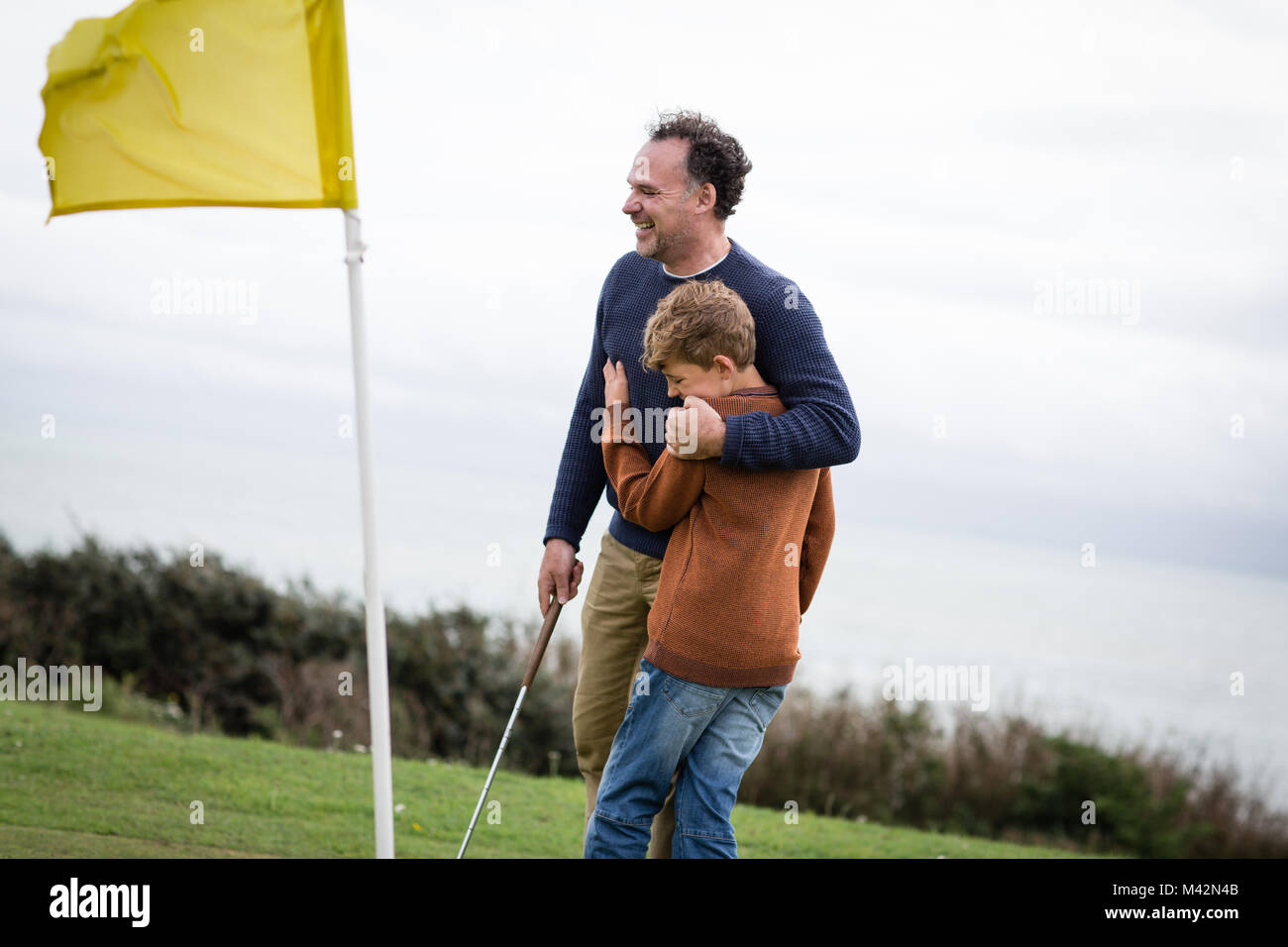 Vater umarmt Sohn auf Golfplatz Stockfoto