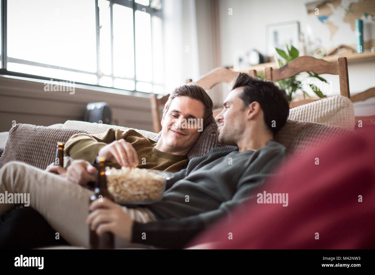 Junge männliche Paar entspannt auf einem Sofa mit Bier und Popcorn Stockfoto