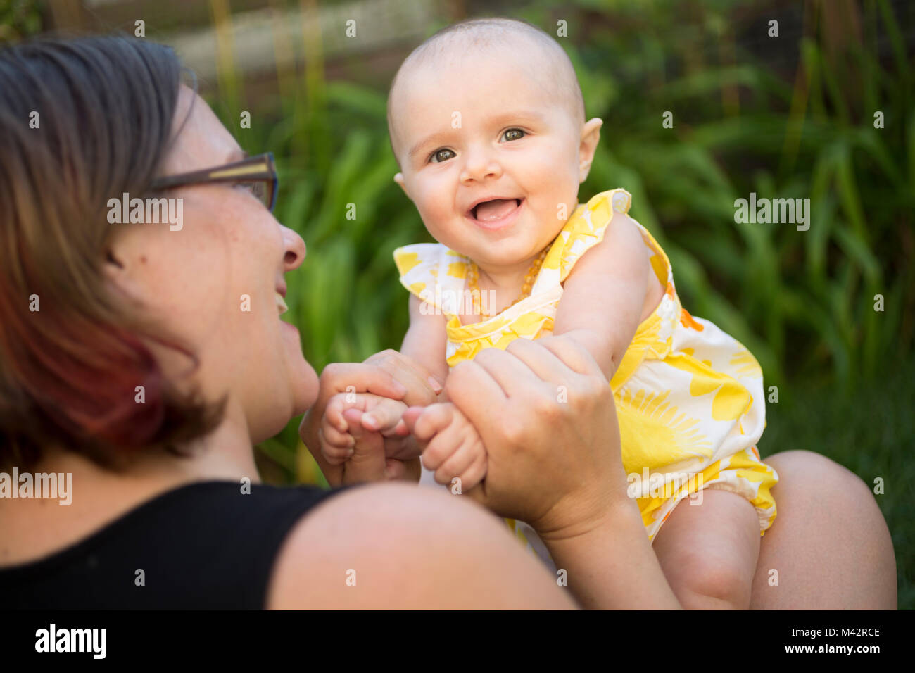 Ein neugeborenes Baby teilt sich ein Lächeln, als er sich mit seiner Mutter in einem Hinterhof Garten. Stockfoto