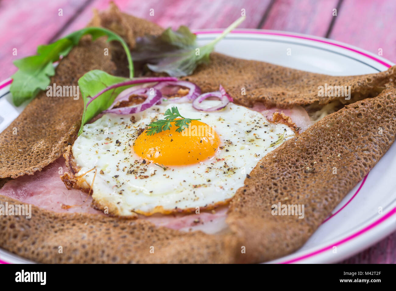 Französische Buchweizen crepe Galette mit Schinken und Ei für leckeres gesundes Mittagessen auf einem rosa Hintergrund Holz Stockfoto