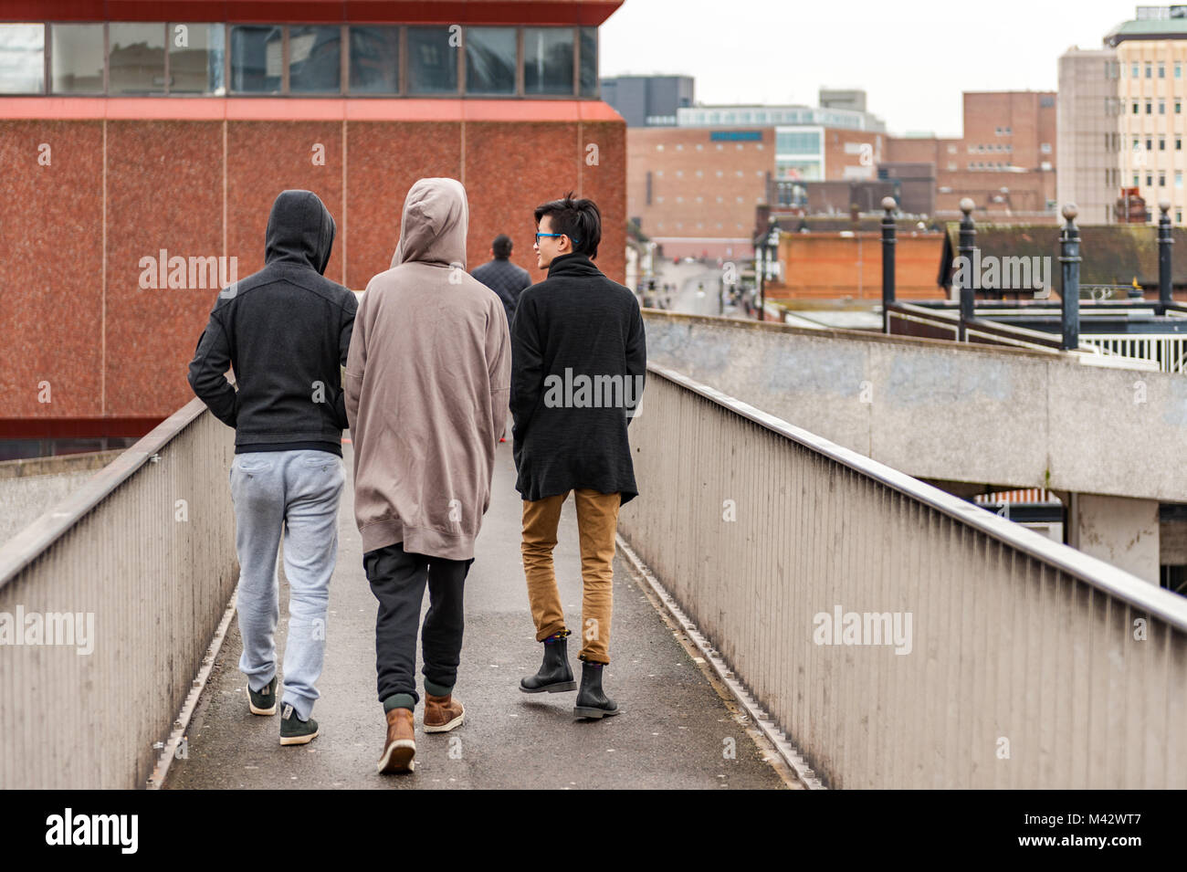 Junge Männer Studenten gehen über eine Fußgängerbrücke in Coventry City Centre, West Midlands, UK. Stockfoto