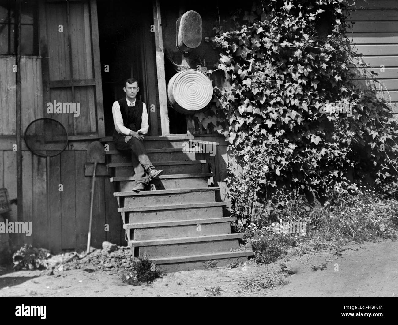 Junger Mann sitzt auf der Treppe von seinen frühen 20. Jahrhunderts amerikanischen Farm Home, Ca. 1915. Stockfoto