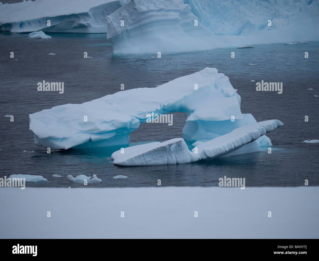 Ein kleiner Eisberg mit einem Torbogen schwebend in Charlotte Bay in der Antarktis. Dichte Wolken sind Gemeinkosten und Stahl grau Wasser in den Vordergrund. Stockfoto