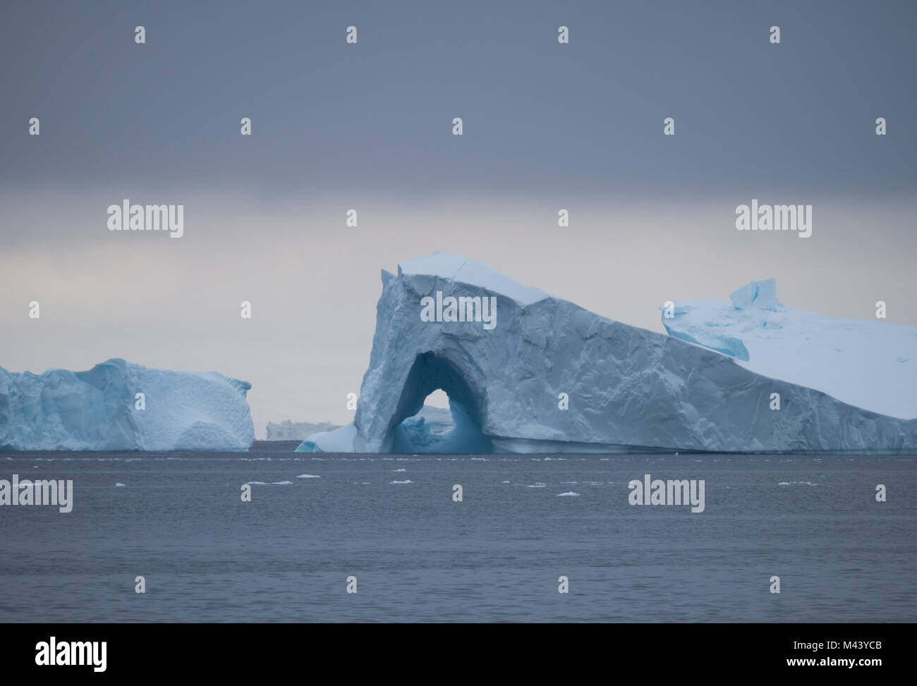 Ein großer Eisberg mit einem Torbogen schwebend in Charlotte Bay in der Antarktis. Dichte Wolken sind Gemeinkosten und Stahl grau Wasser in den Vordergrund. Stockfoto