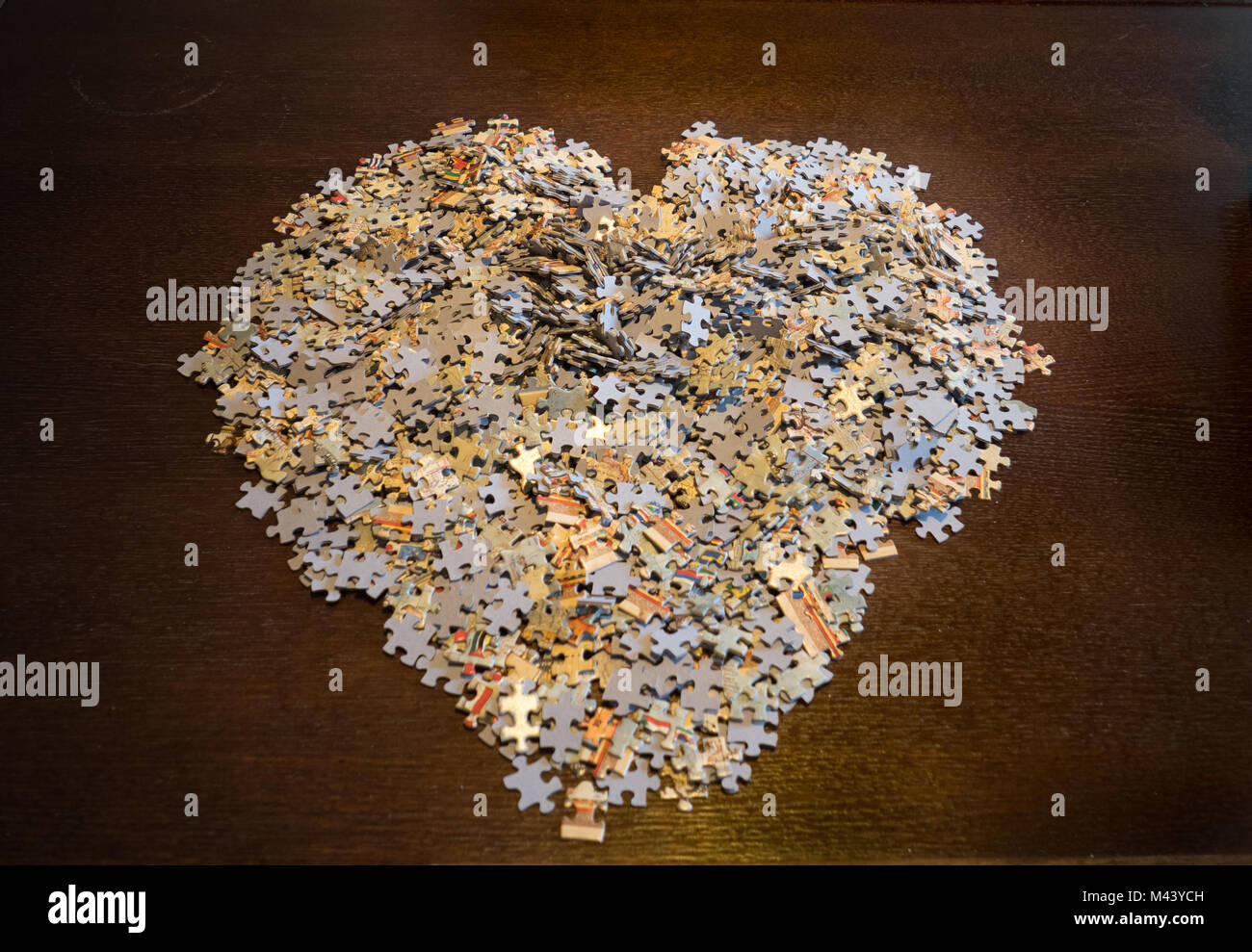 Puzzle Stücke auf einem dunklen Holz Tisch in der Form eines Herzens angehäuft. Stockfoto