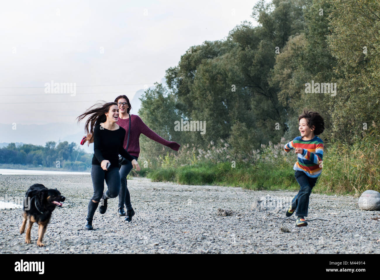 Junge und junge Frauen laufen mit Hund Riverside, Calolziocorte, Lombardei, Italien Stockfoto
