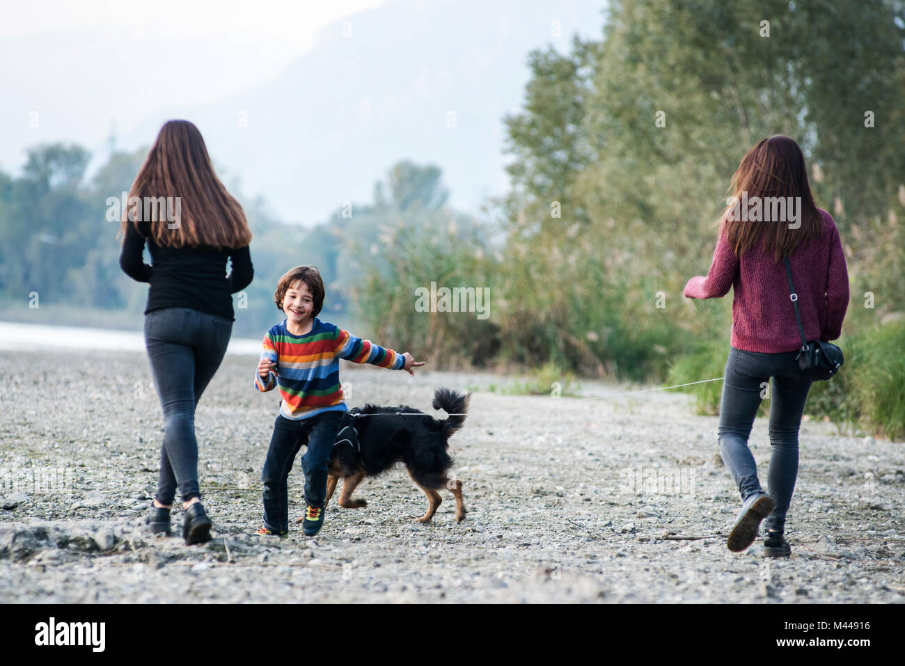 Junge mit jungen Frauen laufen mit Hund Riverside, Calolziocorte, Lombardei, Italien Stockfoto
