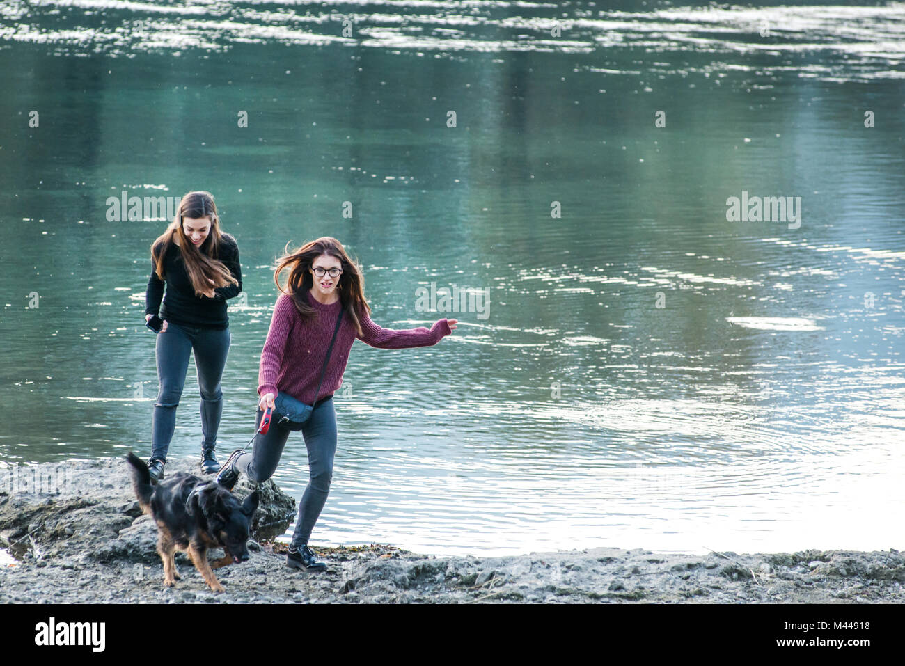 Zwei junge Frauen laufen mit Hund von Fluss, Calolziocorte, Lombardei, Italien Stockfoto