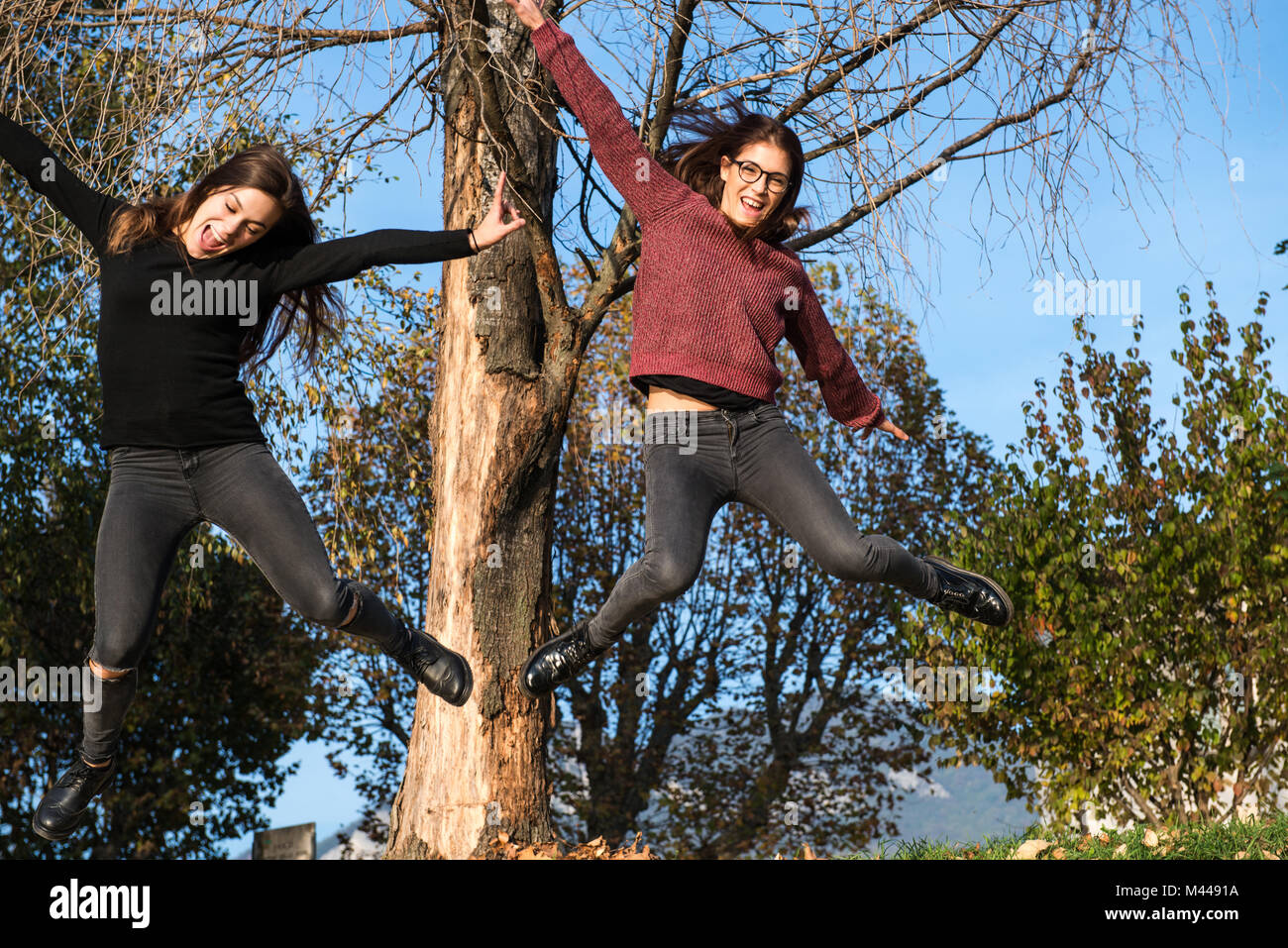 Zwei junge Frauen Springen der Luft in Wäldern, Calolziocorte, Lombardei, Italien Stockfoto