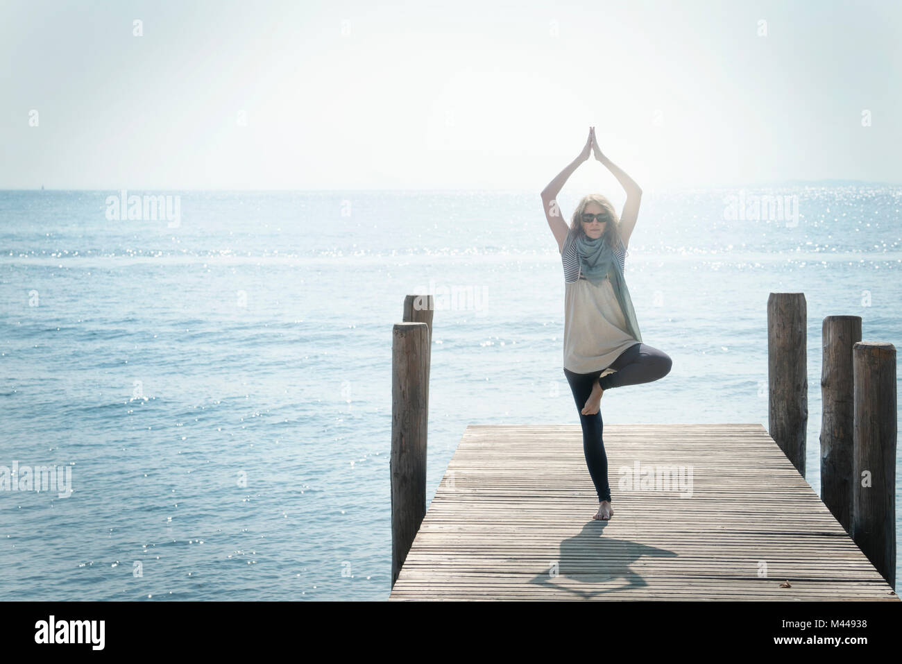 Frau auf Pier auf ein Bein im Yoga pose Stockfoto