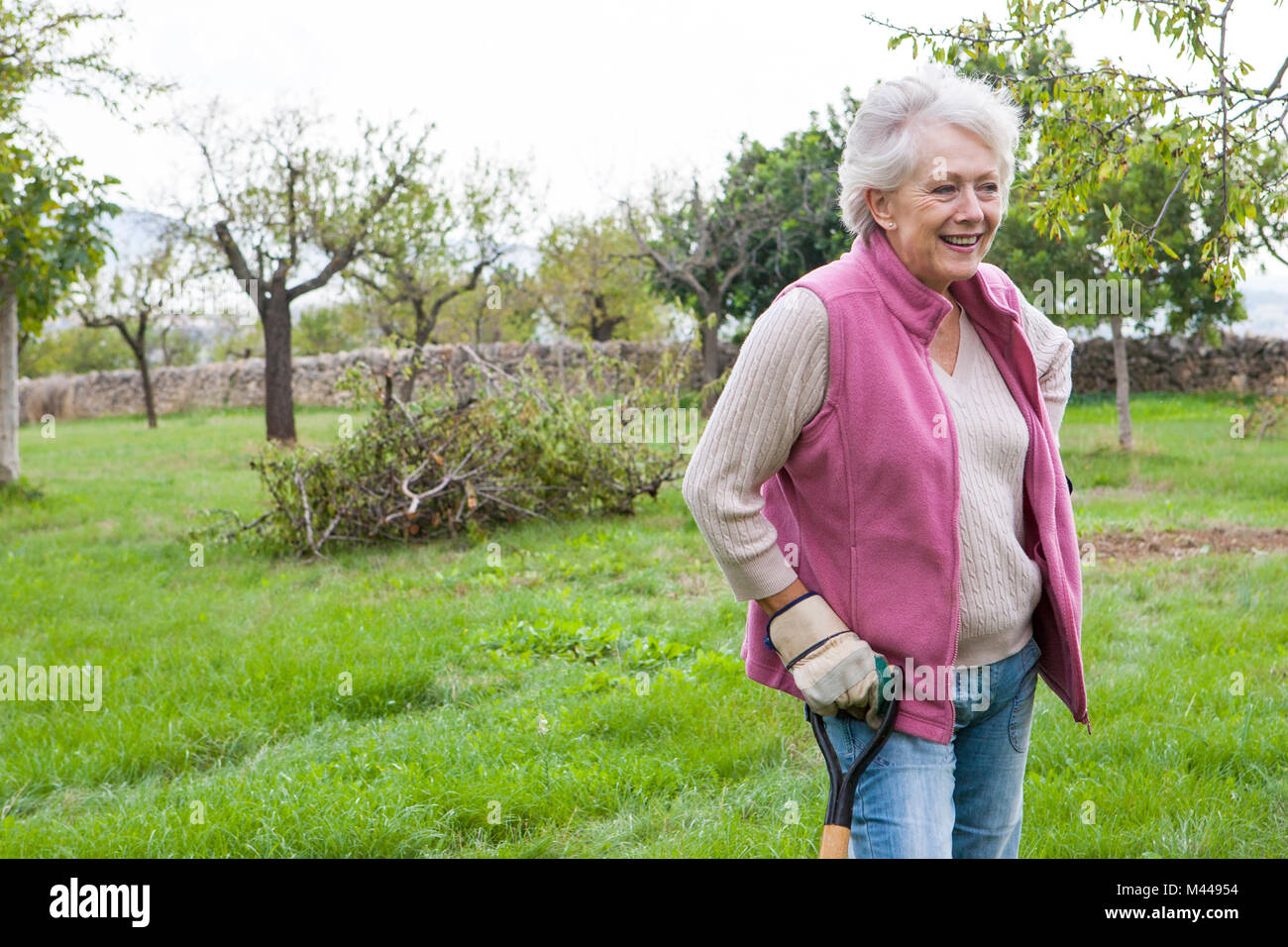 Ältere Frau im Garten, lehnte sich auf Gartengeräte Stockfoto