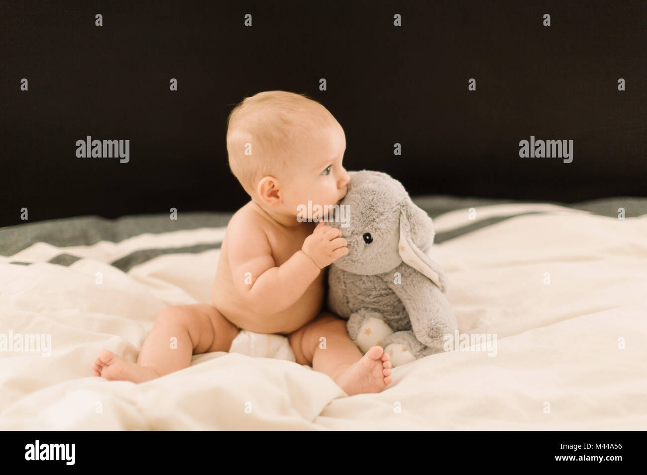 Cute Baby Mädchen sitzt auf dem Bett mit weichen Spielzeug Stockfoto