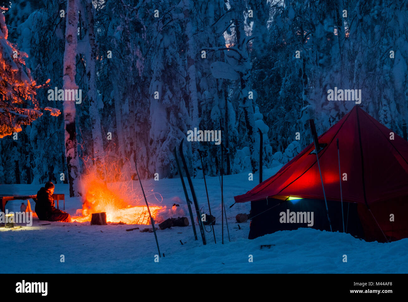 Mann sitzt am Lagerfeuer, in der Nacht, in der Nähe von Zelt, im verschneiten Wald, Russland Stockfoto