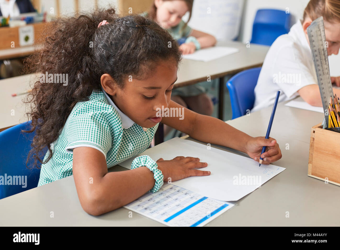 Schülerin schriftlich im Klassenzimmer Schreibtisch in der Grundschule Lektion Stockfoto
