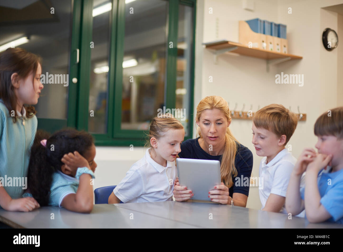 Lehrer mit Schüler und Schülerinnen bei Digital tablet Suchen im Unterricht in der Grundschule Stockfoto