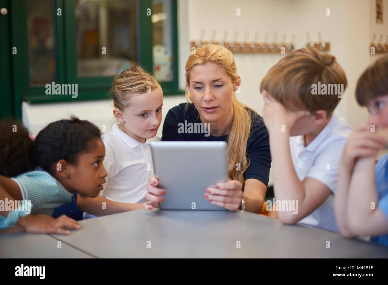 Lehrer mit Schülerinnen und Schüler an den Digitalen tablet Suchen im Unterricht in der Grundschule Stockfoto