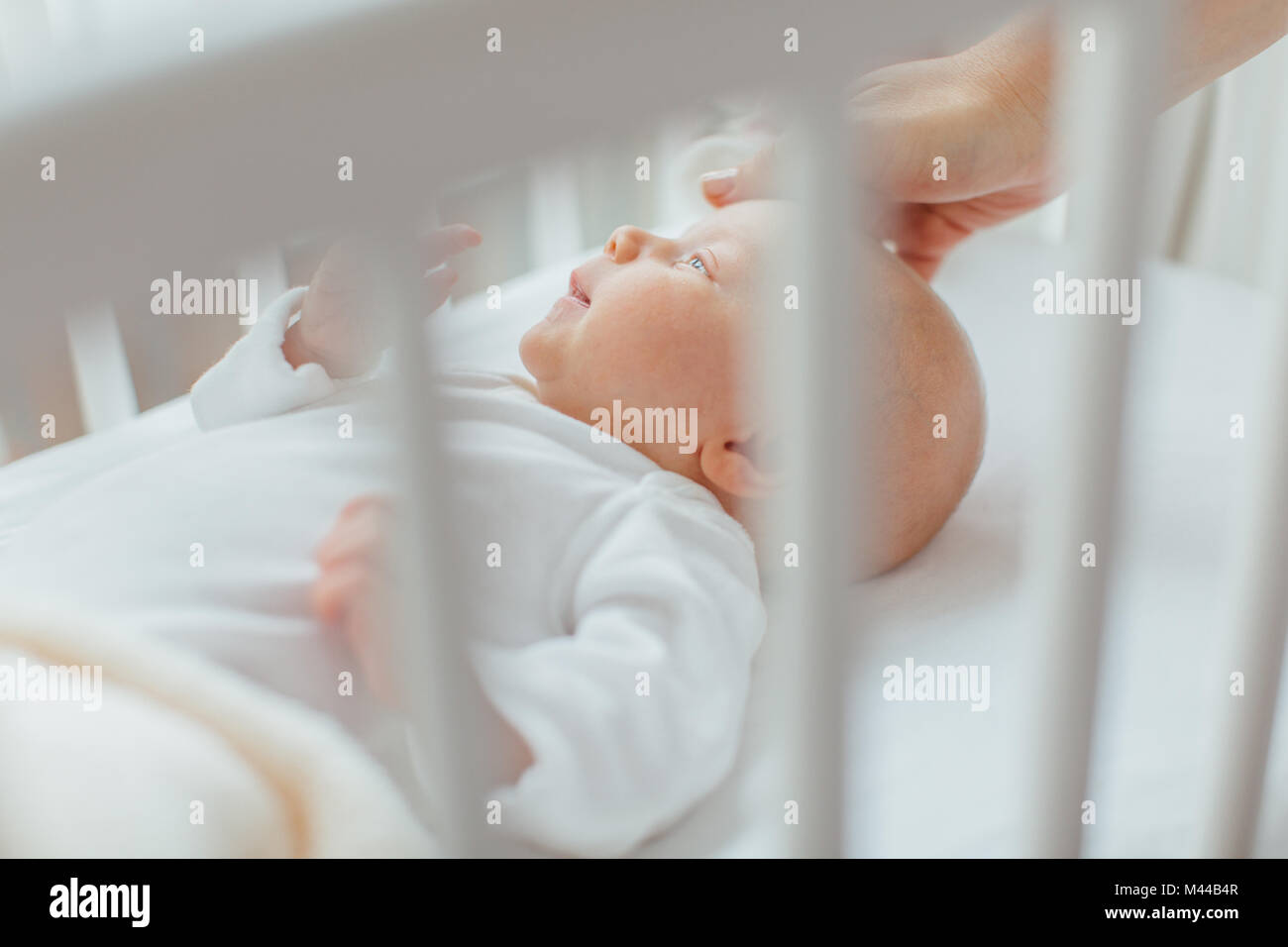 Baby Mädchen in Krippe liegend, Hand's Mutter wohltuende Kopf Stockfoto