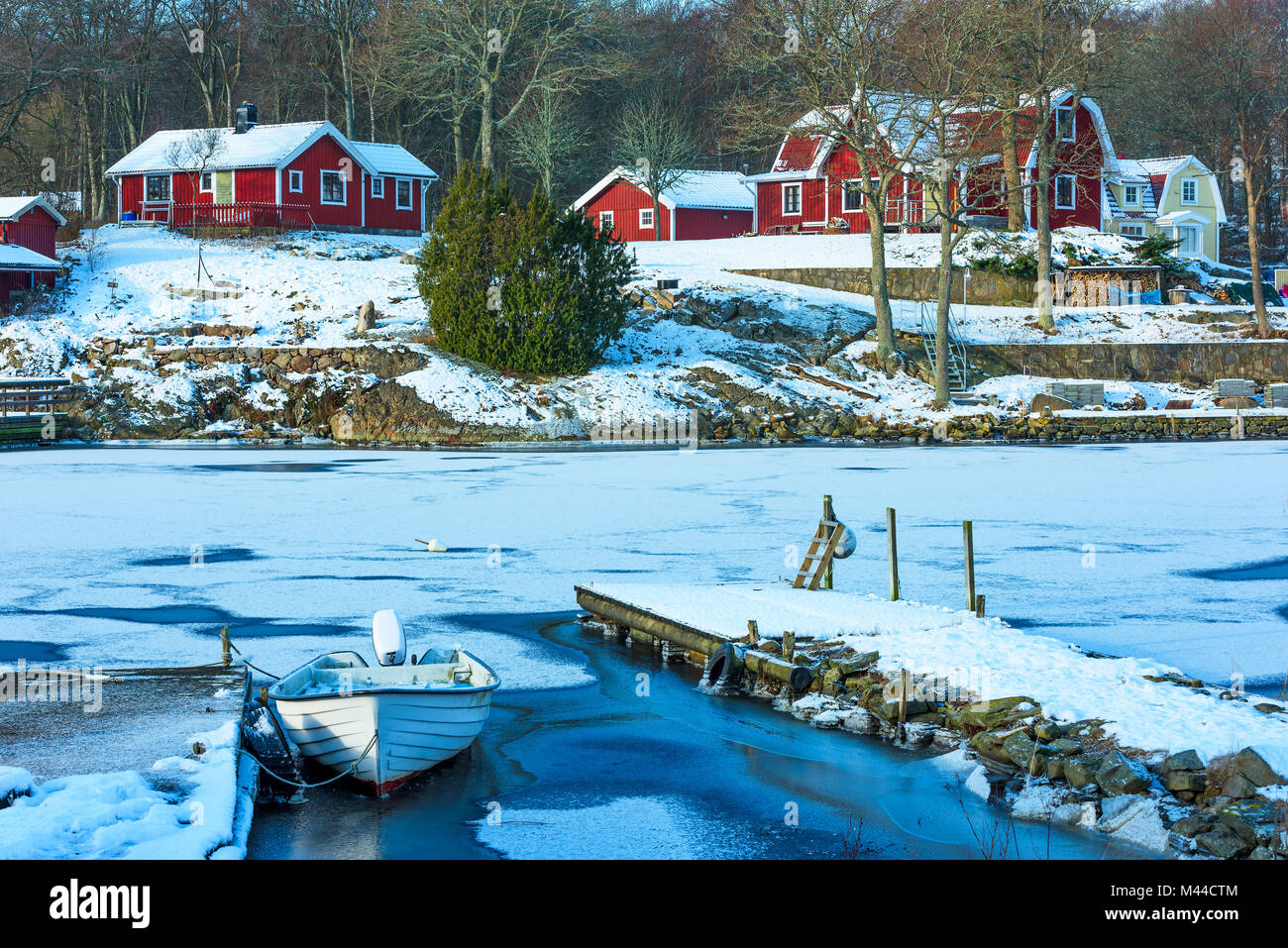 Rote Holzhäuser auf der anderen Seite des gefrorenen Bucht. Kleines Boot vom Steg im Vordergrund eingefroren. Lage Bokevik außerhalb Ronneby im südlichen Sw Stockfoto